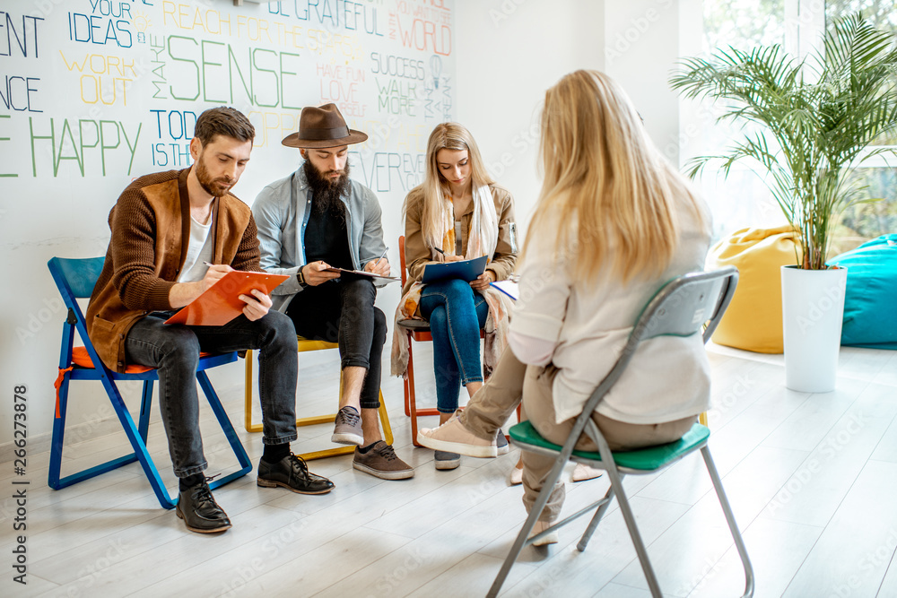 Group of young people sitting together during the psychological therapy with psychologist solving some mental problems in the office Group of young people sitting together during the psychological therapy with psychologist solving some mental problems in the office