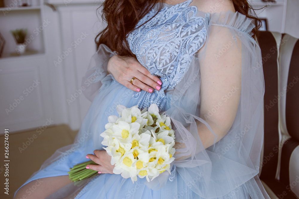 pregnant girl in a blue dress is sitting on a chair with a bouquet of white flowers