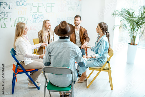 Group of diverse people keeping hands together, sitting in a circle during the psychological therapy, feeling support from each other