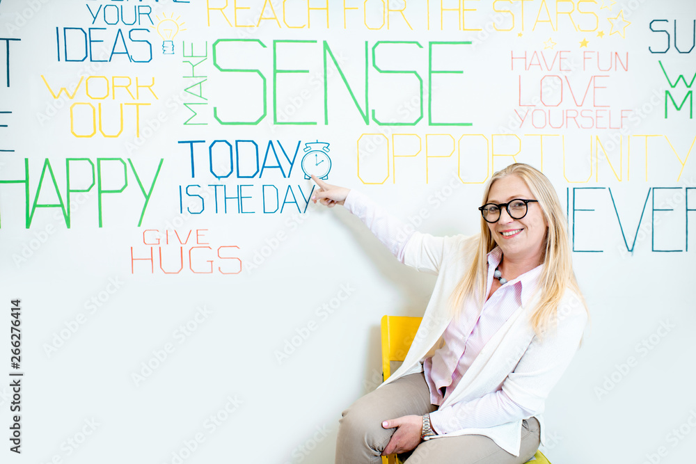 Fototapeta premium Portrait of a senior woman as a mental coach on the wall background with various inscriptions on the topic of mental health indoors