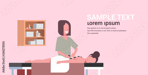 young girl having hot stone massage professional masseuse massaging patient body woman relaxing lying on table luxury spa salon treatments concept horizontal copy space