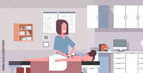 young girl having hot stone massage professional masseuse massaging patient body woman relaxing lying on table medical cabinet interior treatments concept horizontal