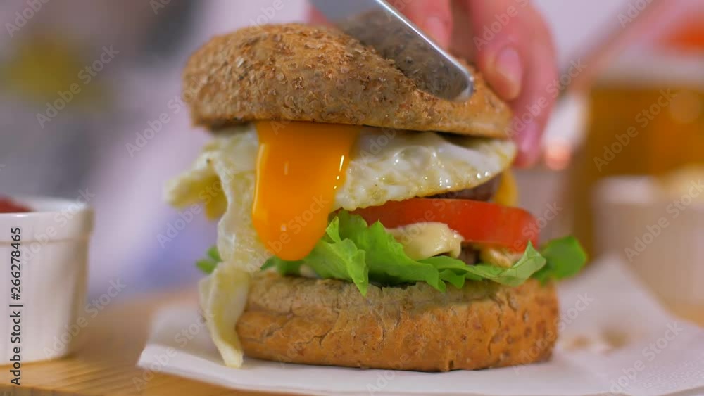 Cutting a juicy American burger. The yolk of the egg is flowing Cutting a juicy American burger. The yolk of the egg is flowing