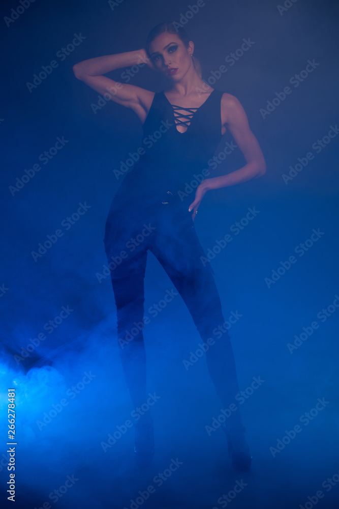 Full length fashon photo of a woman standing over dark background with smoke around her