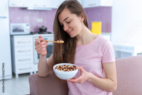 Portrait of young, happy beautiful brunette woman in pajamas eating chocolate balls for cereals breakfast at home