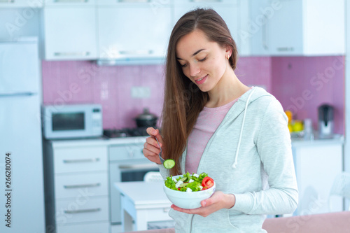 Young happy beautiful vegetarian woman eating vegetables salad for snack at home. Diet and fitness eating. Clean and healthy food