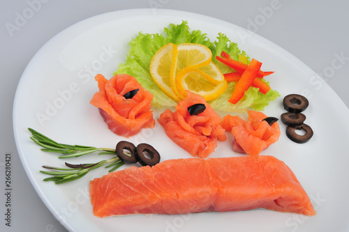 Fresh salmon decorative roses fillets, with lemon, olives on the plate. Isolated on a gray background