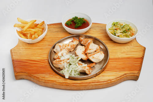 A set of french fries, salad, sauce and fried pieces of meat on a board on a gray isolated background