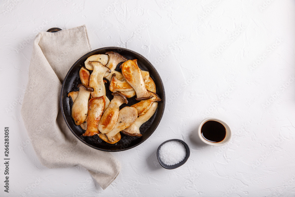 Fried eryngii mushrooms in cast-iron pan on white table. Grilled slices of king oyster mushrooms. Top view, copy space. Fried eryngii mushrooms in cast-iron pan on white table. Grilled slices of king oyster mushrooms. Top view, copy space.