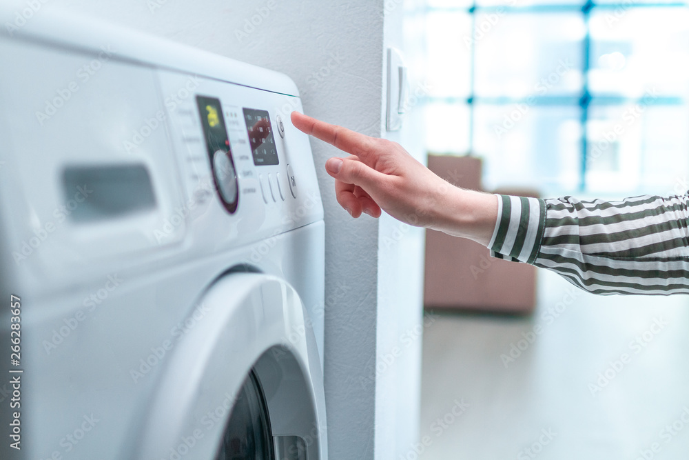 Housewife using display and button for turning on and choosing cycle program on washing machine for laundry at home. Housewife using display and button for turning on and choosing cycle program on washing machine for laundry at home.