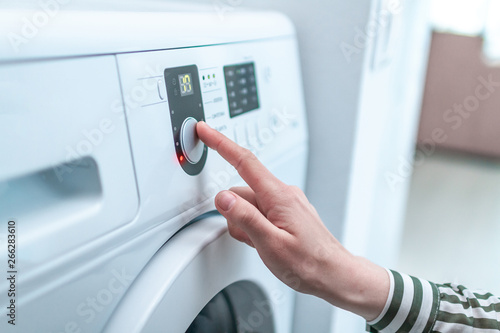Housewife using display and button for turning on and choosing cycle program on washing machine for laundry at home.