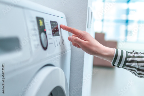 Fotografía Housewife using display and button for turning on and choosing cycle program on washing machine for laundry at home