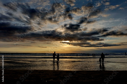 tourists while enjoying the sunset on Kuta beach  with an exciting atmosphere  the color of the sky is golden and the weather is sunny  so visitors are very comfortable to linger