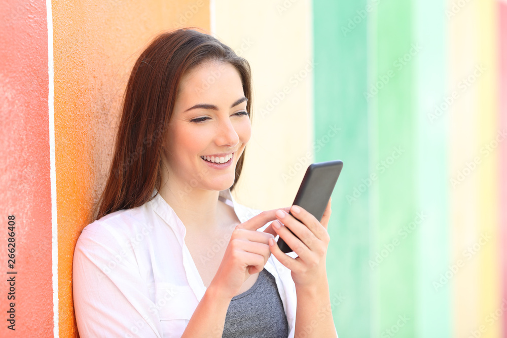 Happy girl browsing phone content in a colorful street Happy girl browsing phone content in a colorful street
