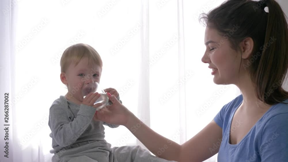 baby care, crying child boy drinking pure mineral water from glass from young mom arms to quenching of thirst close up in natural light at home baby care, crying child boy drinking pure mineral water from glass from young mom arms to quenching of thirst close up in natural light at home