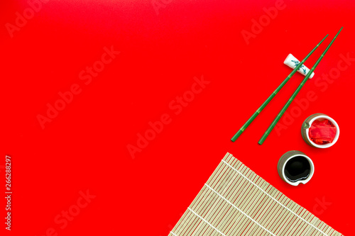 oriental table set up with bamboo sticks for sushi and maki, soy sauce on red background top view space for text