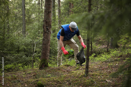 Man cleans garbage and plastic bottle in forest. Green volunteering. Caring for environment.