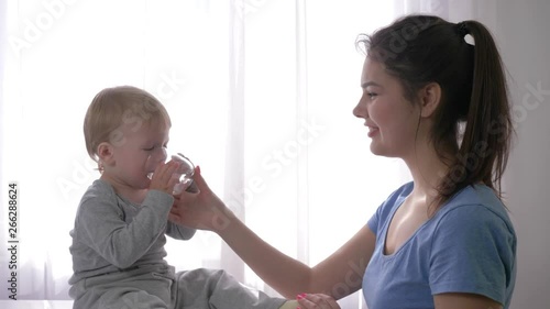 casualty, sweet infant boy choked on water and coughing while drinking from glass to quench thirst and near young mother helped her son close up in natural light indoors photo