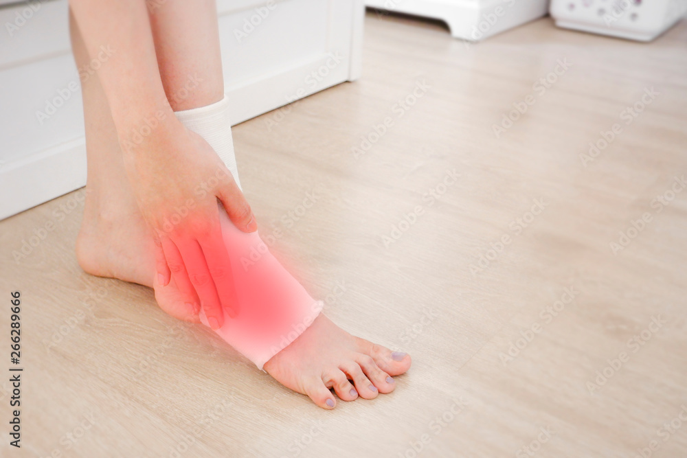 Closeup of a Foot with Gauze Elastic Bandage. Asian Woman Ankle Injury Runner. Hands on Injured Legs and Feet with Red Spot on Pain Area Sitting on a Wooden Floor Background from Rupture or Tear.