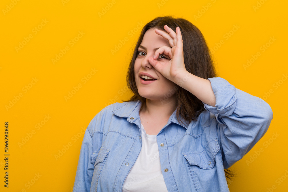 Young curvy plus size woman excited keeping ok gesture on eye. Young curvy plus size woman excited keeping ok gesture on eye.