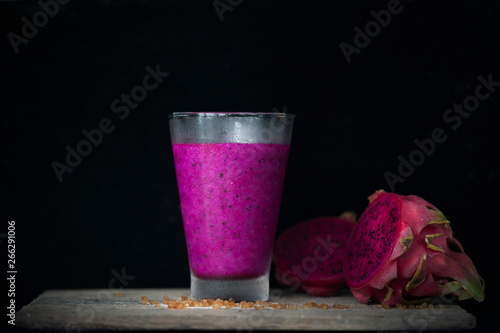 Red Dragon fruit juice on wooden surface, solid black background, still life shooting style.
