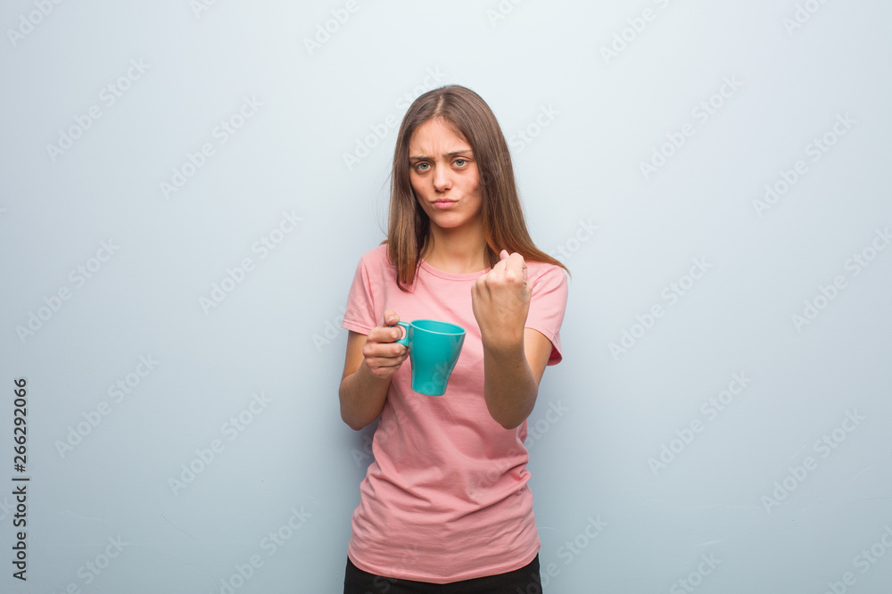 Young pretty caucasian woman showing fist to front, angry expression. She is holding a mug. Young pretty caucasian woman showing fist to front, angry expression. She is holding a mug.