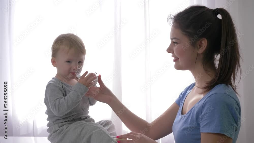 young mother gives little son glass of mineral water to quench thirst and baby is very happy and laughing close up in natural light at home. young mother gives little son glass of mineral water to quench thirst and baby is very happy and laughing close up in natural light at home.