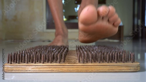 Male feet step on a wooden yoga board with lot of metal nails pins. Close up of yoga board with sharp nails photo