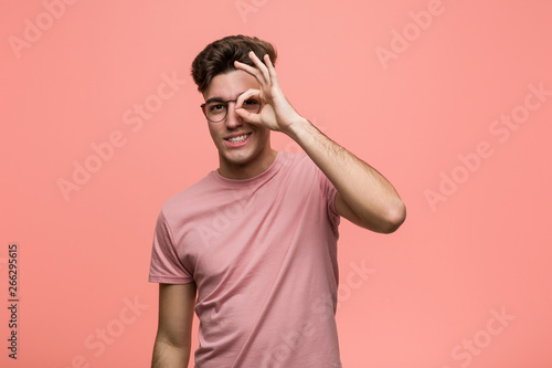 Young cool caucasian man excited keeping ok gesture on eye.