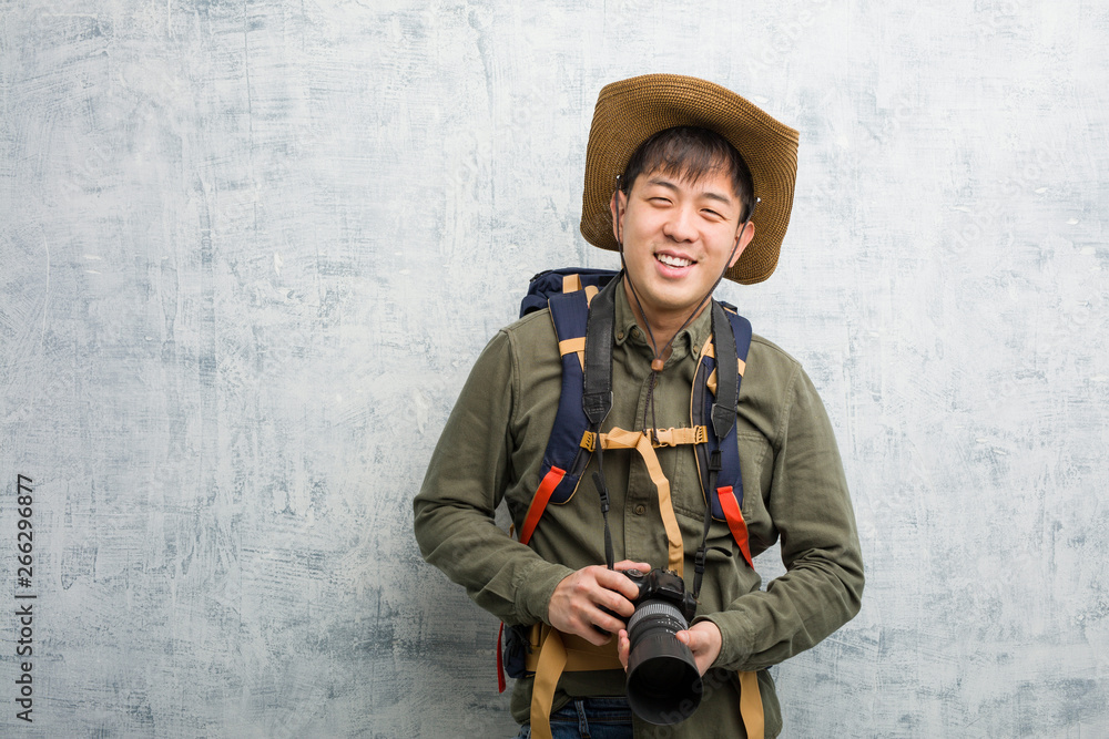 Fototapeta premium Young chinese explorer man holding a camera cheerful with a big smile