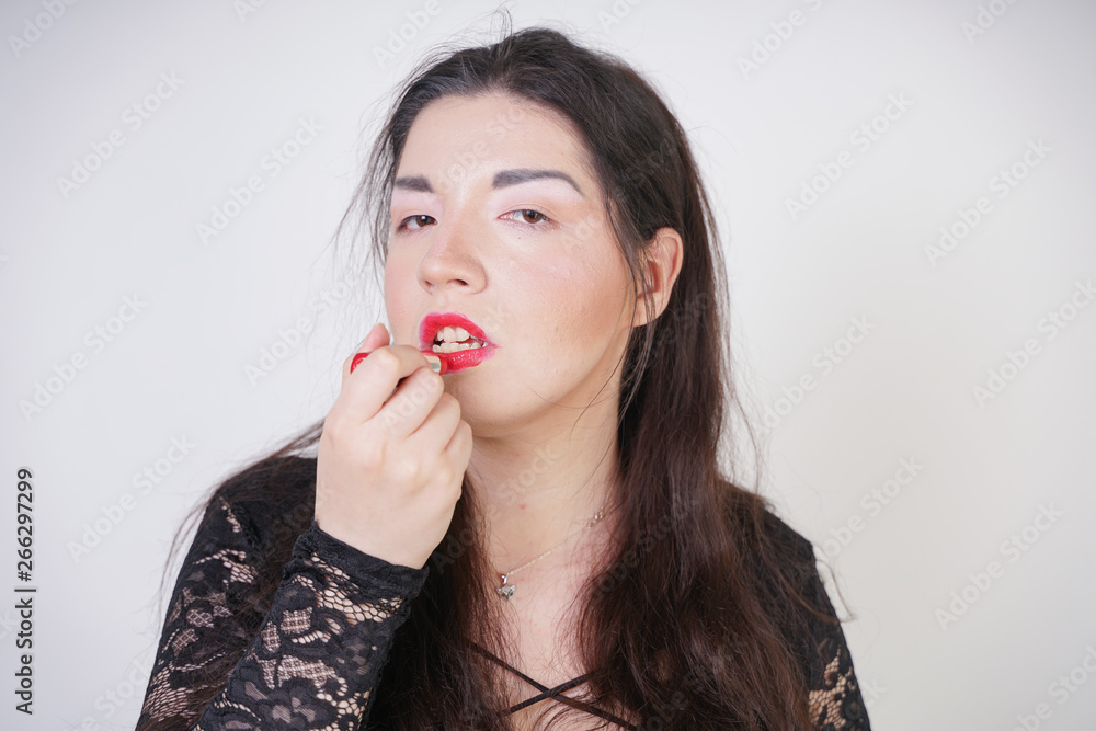 Asian happy woman paints her lips with lipstick on white studio background. Wrong try to do good self make up. Adult girl is learning to paint her face. Asian happy woman paints her lips with lipstick on white studio background. Wrong try to do good self make up. Adult girl is learning to paint her face.
