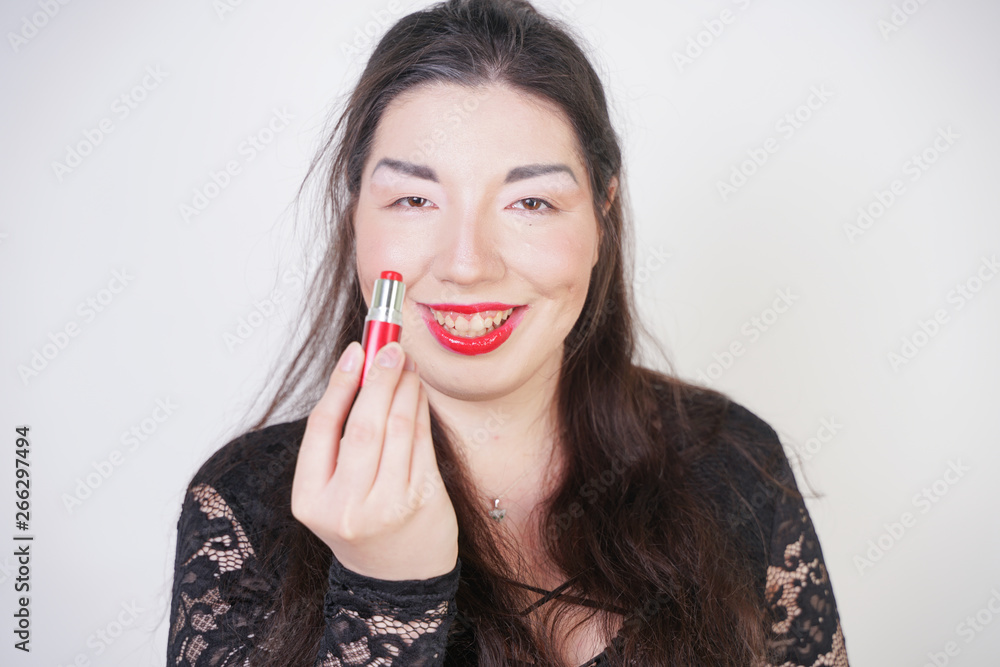 Asian happy woman paints her lips with lipstick on white studio background. Wrong try to do good self make up. Adult girl is learning to paint her face. Asian happy woman paints her lips with lipstick on white studio background. Wrong try to do good self make up. Adult girl is learning to paint her face.