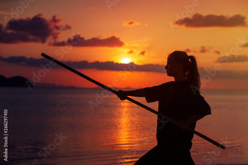 Young beautiful girl woman blond doing kung fu with bamboo stick on the seashore at sunset © olezzo