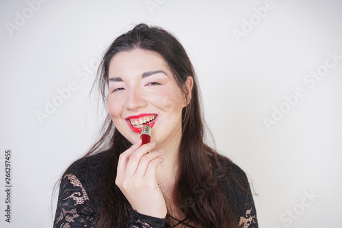 Asian happy woman paints her lips with lipstick on white studio background. Wrong try to do good self make up. Adult girl is learning to paint her face.