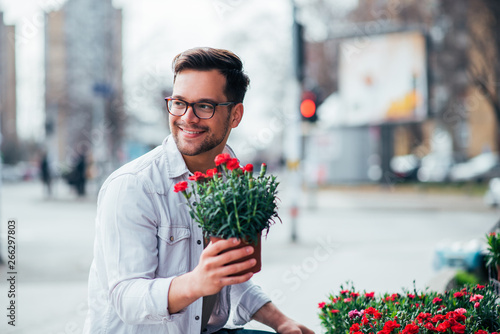 Positive young man buying flowers outdoors. photo