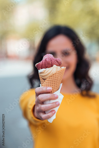 Obraz na plátne Young woman holding ice cream cone toward camera, focus on the foreground