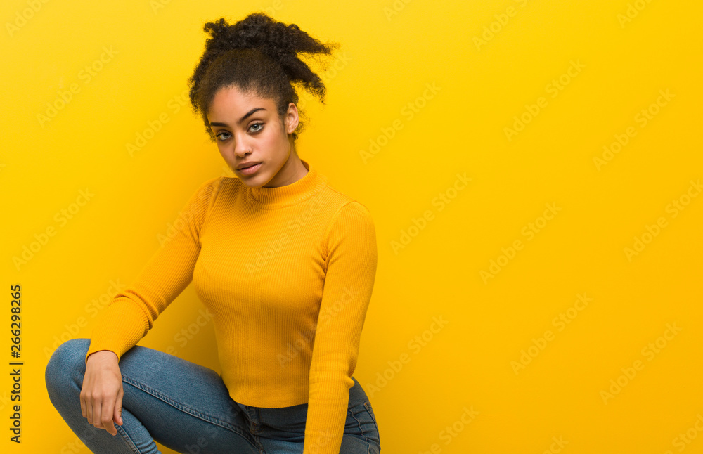 Young black woman sitting over an orange wall Young black woman sitting over an orange wall