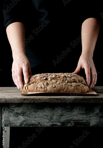 female hands hold oval baked rye bread with pumpkin seeds