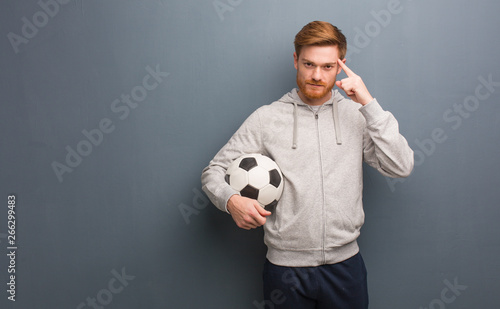 Young redhead fitness man thinking about an idea. He is holding a soccer ball.