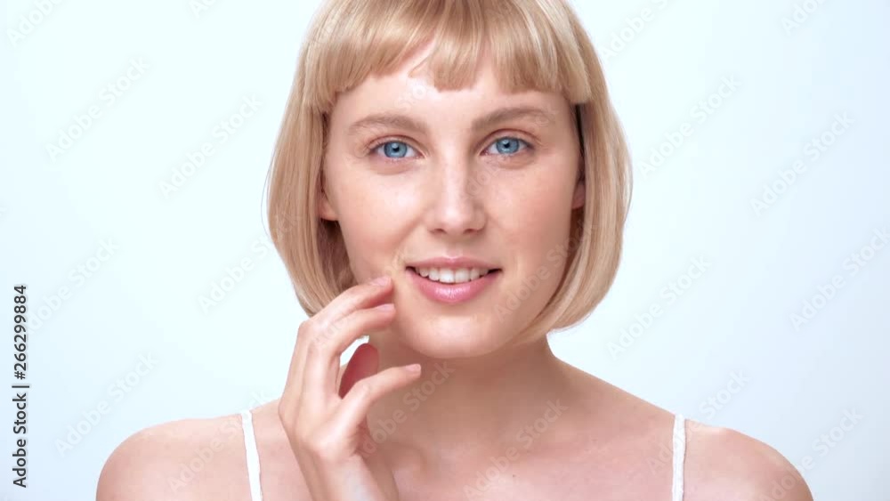 A beautiful caucasian female with blue eyes, blonde hair and a cute smile looks into the camera and gently touches her face for a beauty shoot in the studio on a white background. A beautiful caucasian female with blue eyes, blonde hair and a cute smile looks into the camera and gently touches her face for a beauty shoot in the studio on a white background.