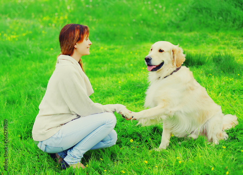 Happy woman owner is training her Golden Retriever dog on grass, giving paw to hand