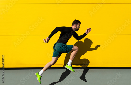 Obraz na plátně Portrait of male athlete running isolated on yellow wall.