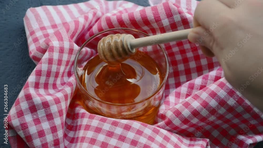Viscous liquid honey flows into a glass jar with honey sticks. Honey in glass jar and honey stick Viscous liquid honey flows into a glass jar with honey sticks. Honey in glass jar and honey stick