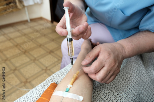 The nurse enters a medical syringe into the system of tubes in the hand of a woman who is lying. The concept of medical procedure.