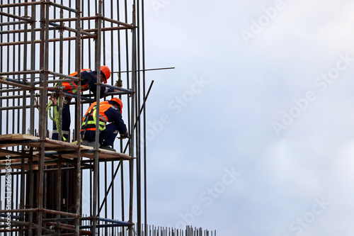 Construction workers on scaffolding. Installers working on a building frame against the cloudy blue sky