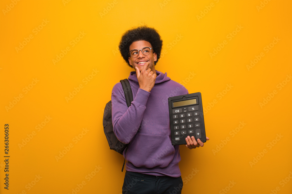 Young african american student man holding a calculator relaxed thinking about something looking at a copy space - obrazy, fototapety, plakaty 