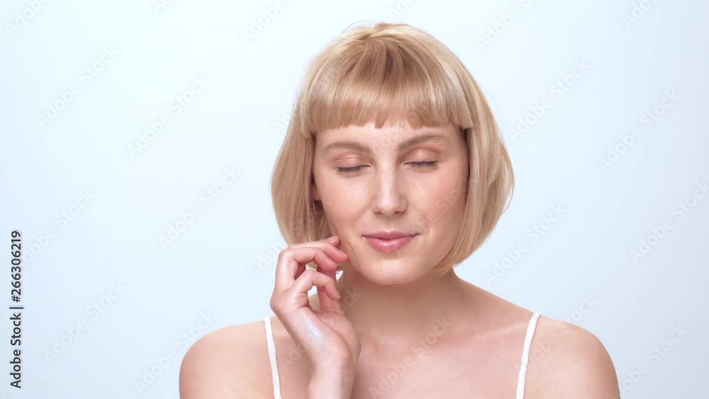 A beautiful caucasian woman with blue eyes, blonde hair and a cute smile looks into the camera and gently touches her face for a beauty shoot in the studio on a white background. A beautiful caucasian woman with blue eyes, blonde hair and a cute smile looks into the camera and gently touches her face for a beauty shoot in the studio on a white background.