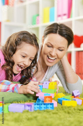 Curly little girl and her mother playing with colorful plastic blocks