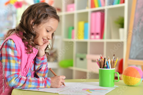 Cute little girl drawing while sitting at table