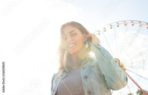 Close up of a smiling relaxed young blond looking away at the park Ferris wheel on background. Happy woman in sunlight